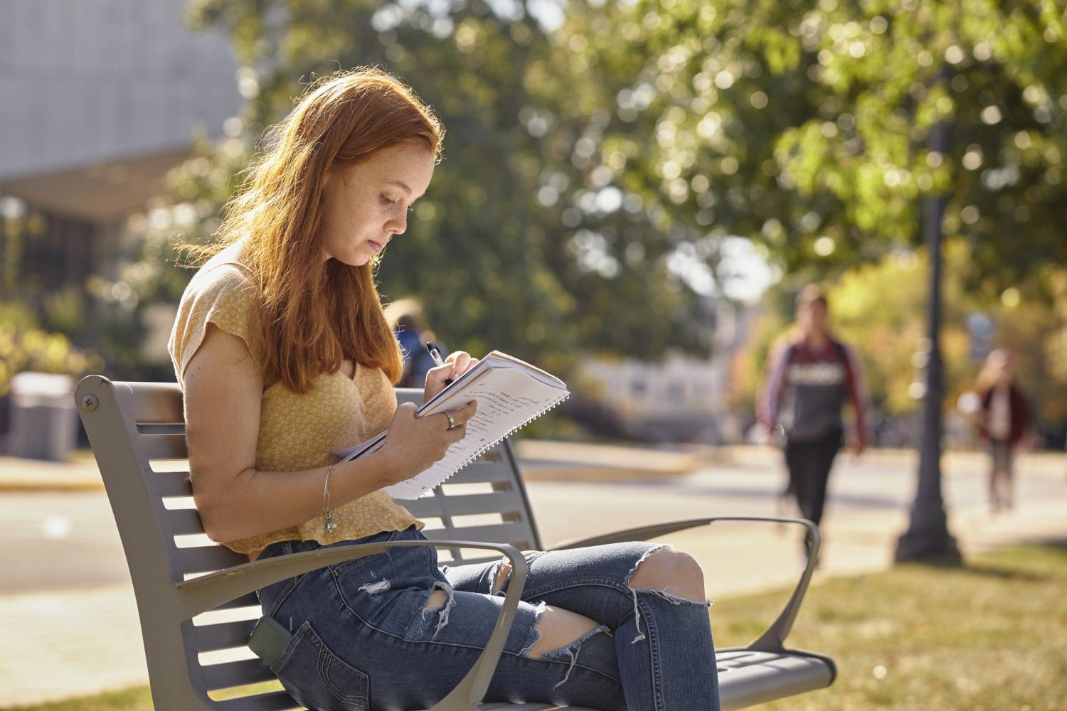 A Carthage College student reads on a bench along Campus Drive.